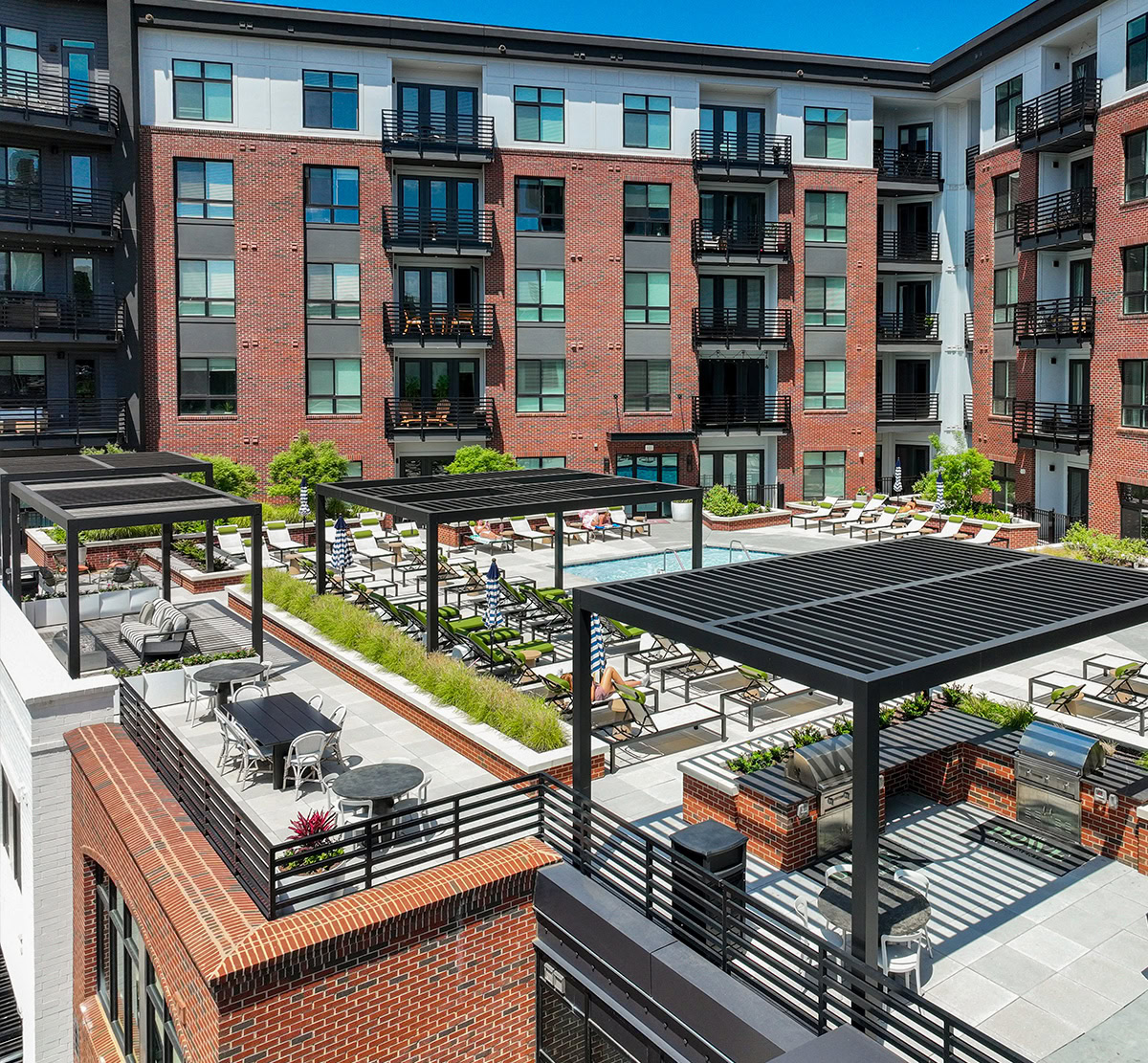 Rooftop courtyard with a pool, lounge chairs, pergolas, grilling areas, and surrounding apartment balconies.